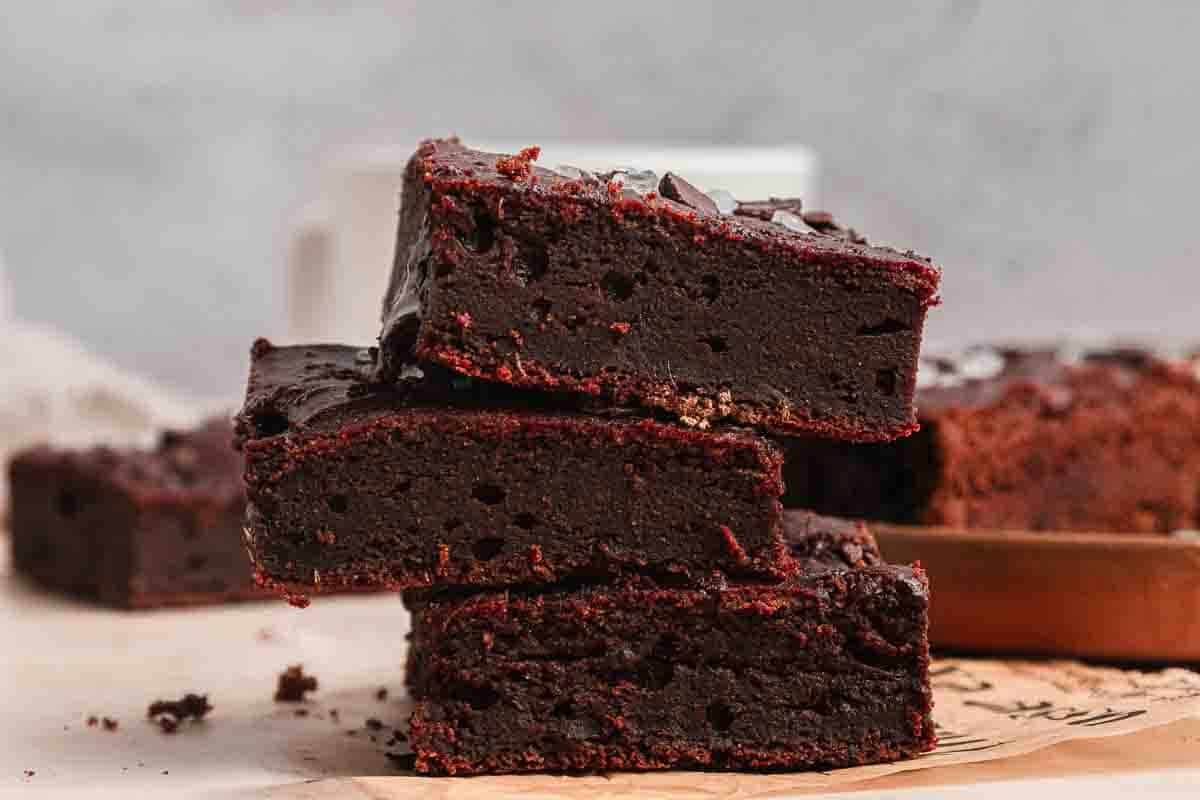 Three thick, fudgy chocolate brownies stacked on top of each other on a parchment surface.
