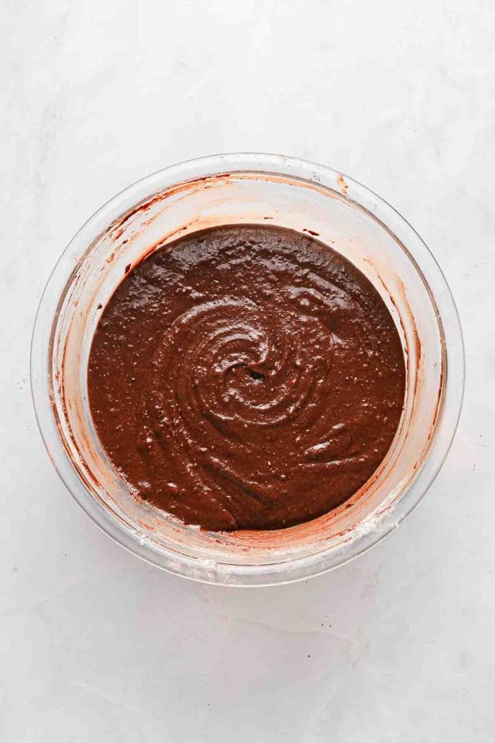 A glass bowl filled with chocolate cake batter on a white surface.