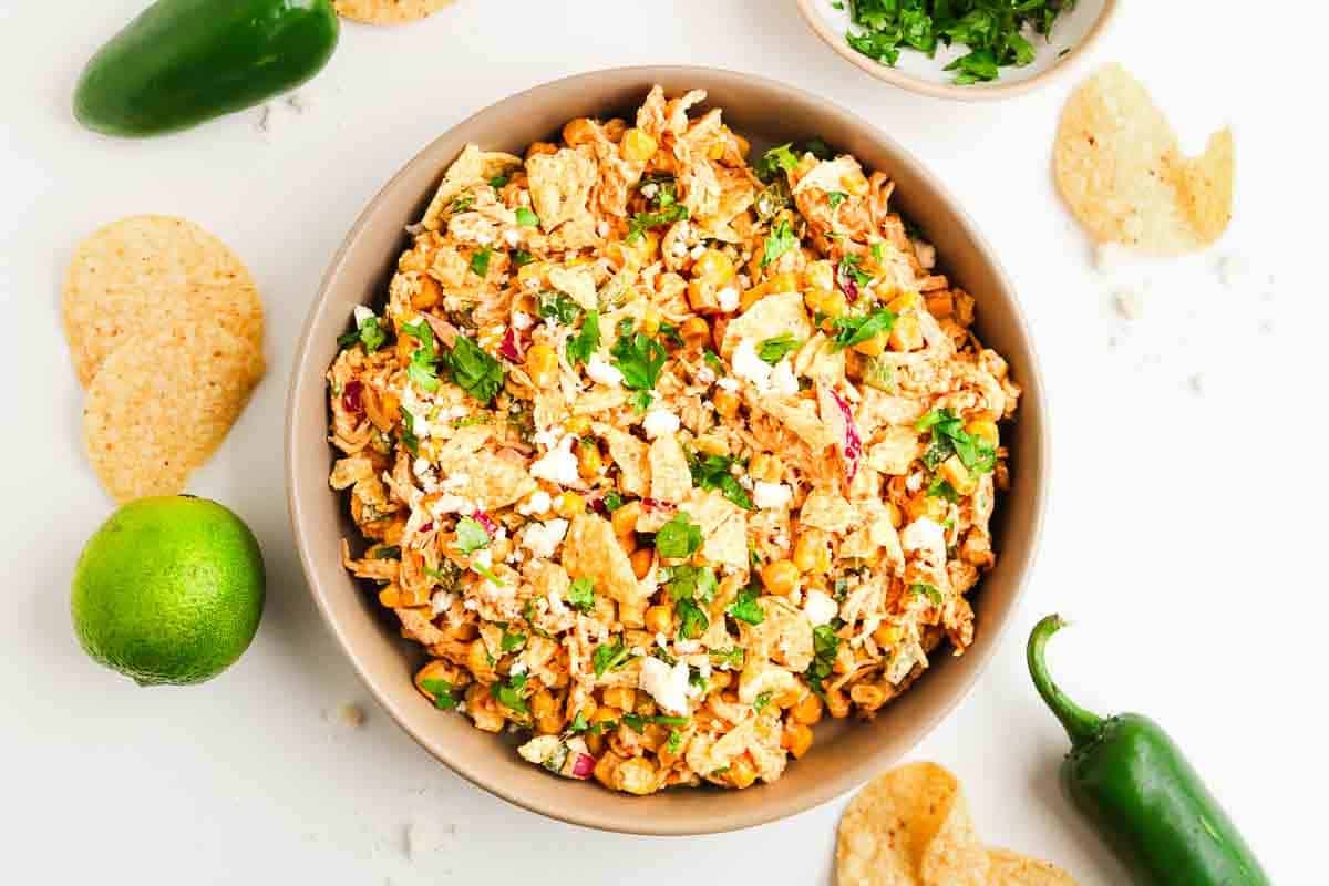 Bowl of taco salad with chips, lime, jalape&ntilde;os, and fresh herbs on a white background.