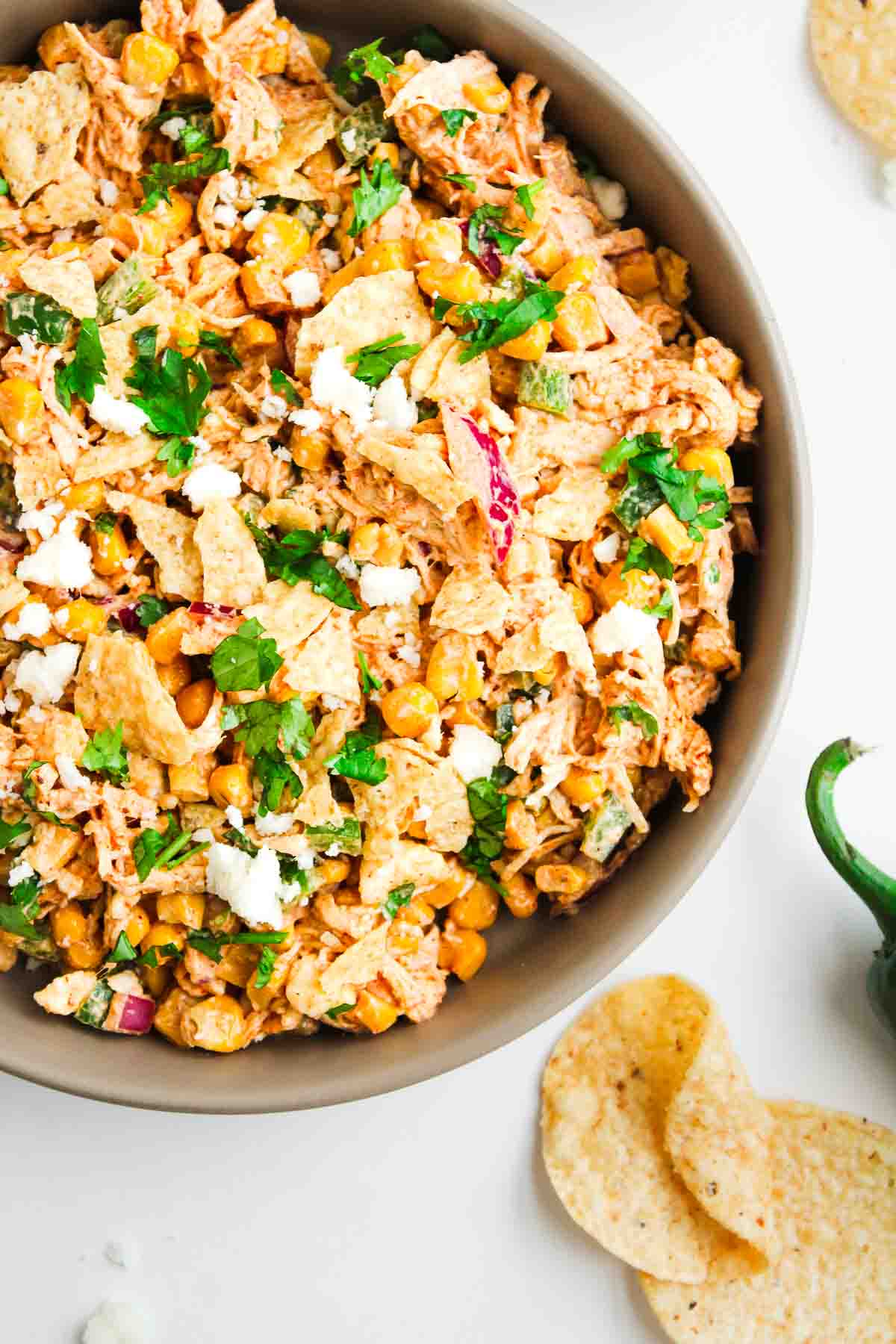 A bowl of Mexican street corn chicken salad topped with cilantro, tortilla chips, and crumbled cheese.