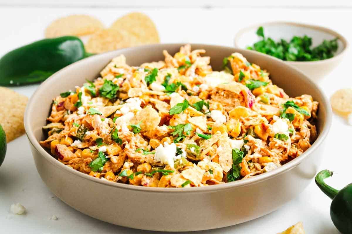 A bowl of chicken chilaquiles topped with fresh cilantro and crumbled cheese, surrounded by tortilla chips.