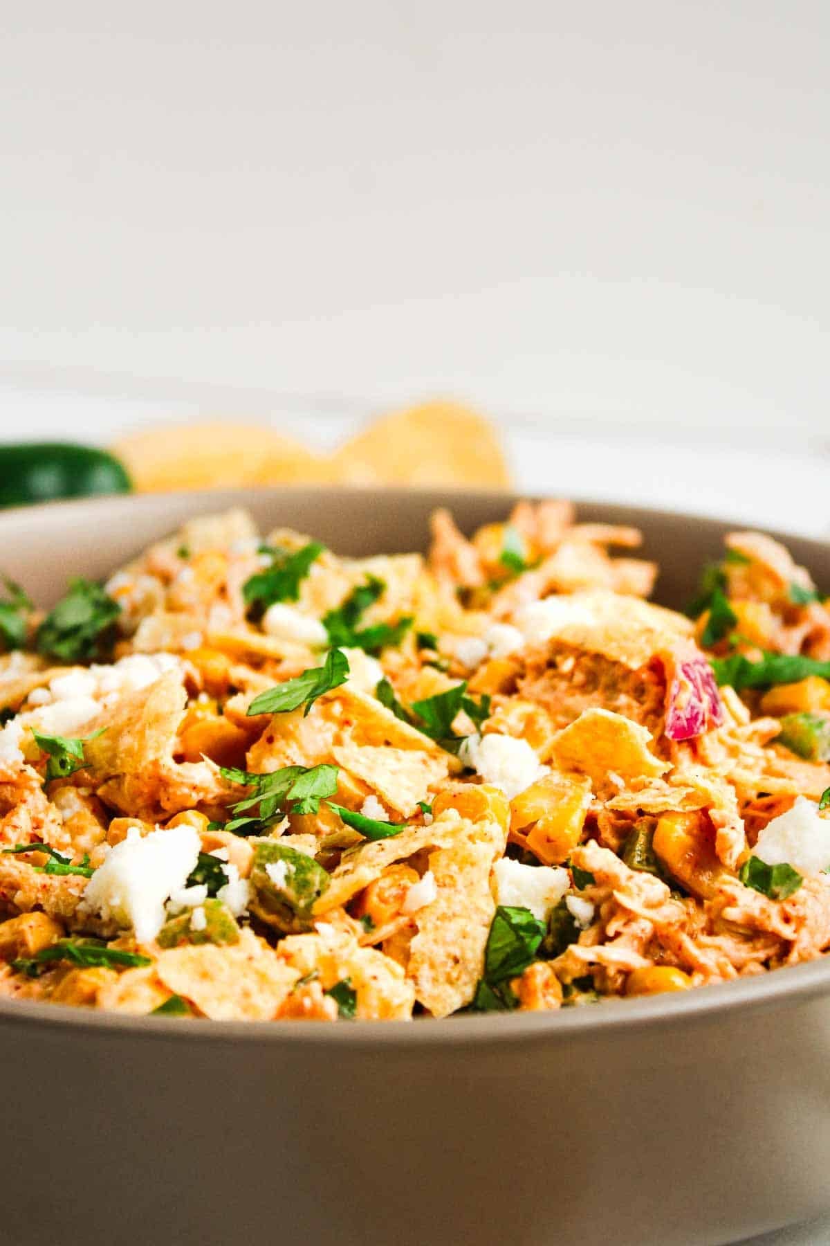 Bowl of Mexican chicken salad topped with crushed tortilla chips, fresh cilantro, and crumbled cheese.