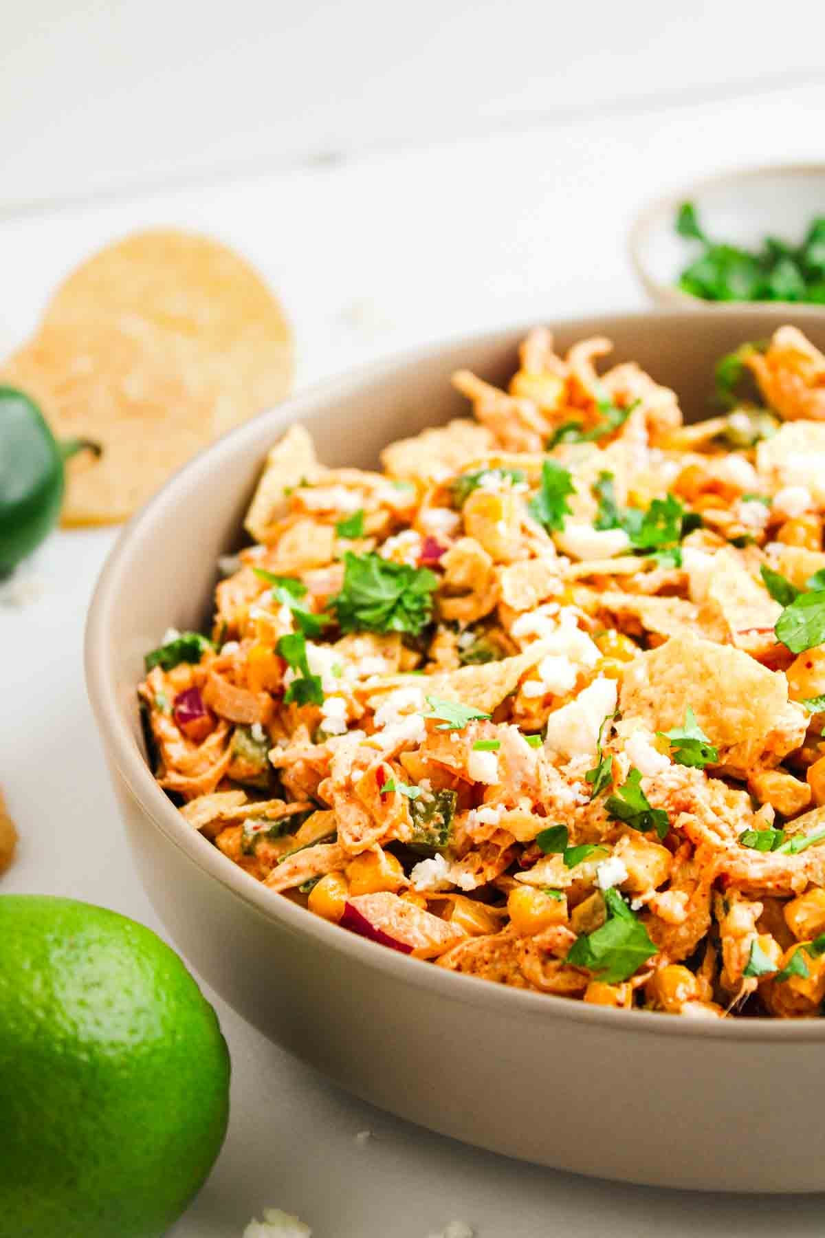 A bowl of Southwest-style salad with cilantro, corn, cheese, tortilla strips, and fresh lime nearby.