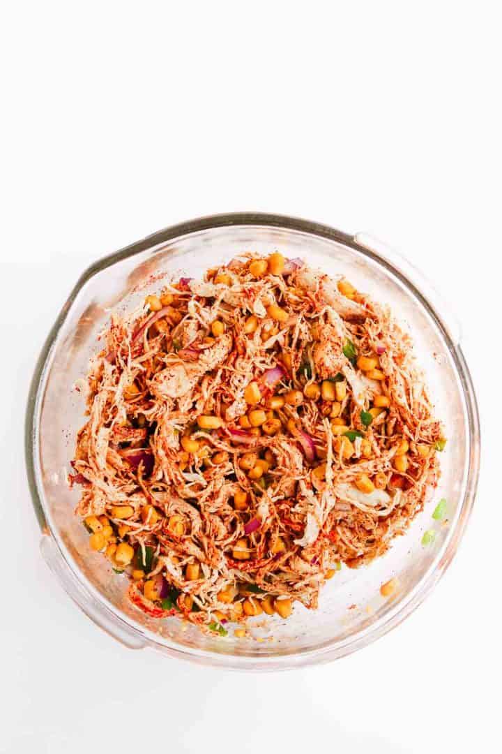 Shredded chicken mixed with chickpeas, red onions, and herbs in a glass bowl on a white background.