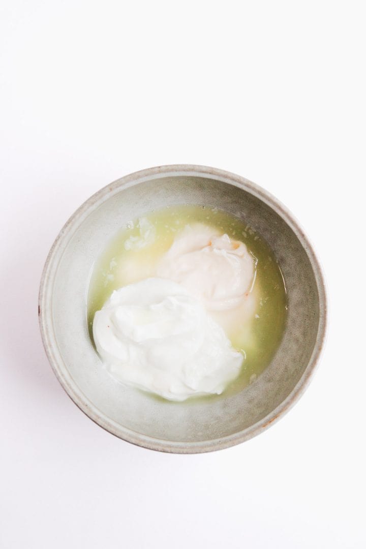 A bowl with a mixture of white yogurt and yellowish liquid on a white background.