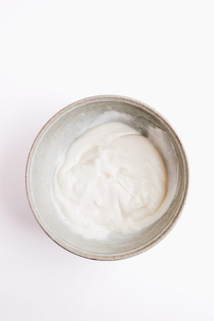 A gray bowl filled with plain, creamy white yogurt on a white background.