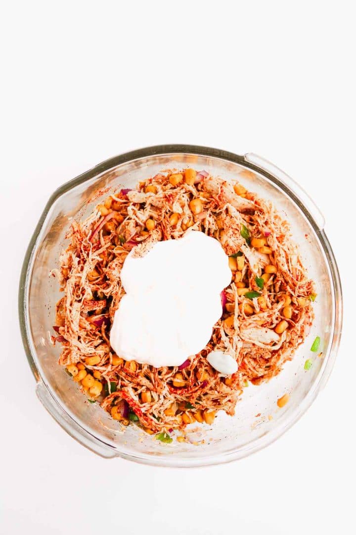 Glass bowl filled with shredded chicken, beans, vegetables, and a dollop of sour cream on top.