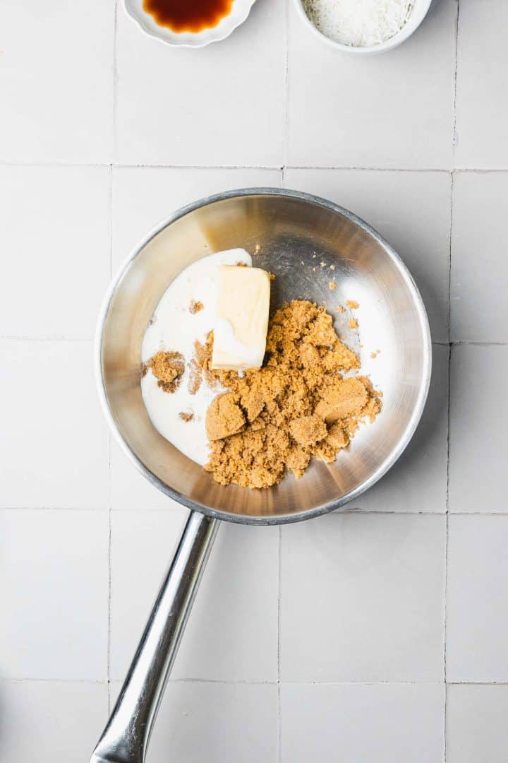 A saucepan with brown sugar, butter, and cream, on a light tiled surface.