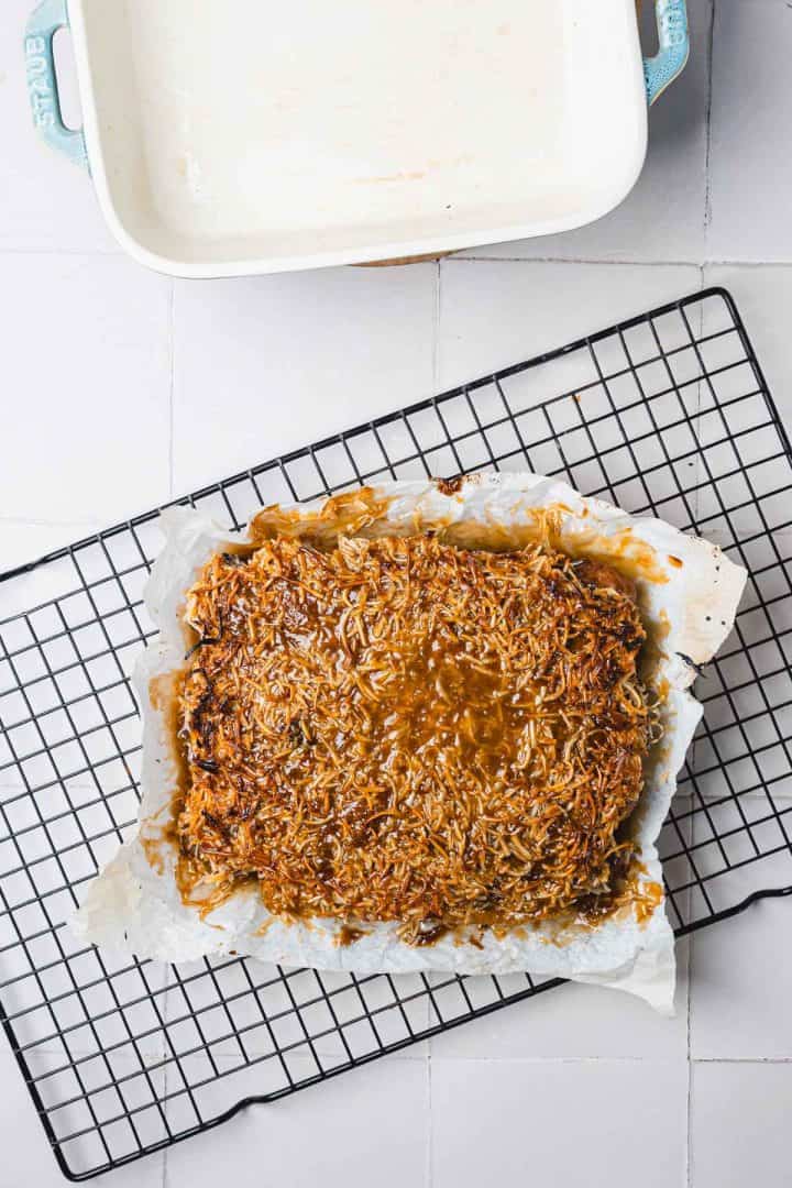 A baked oat and coconut bar slab on parchment paper, cooling on a wire rack near an empty baking dish.