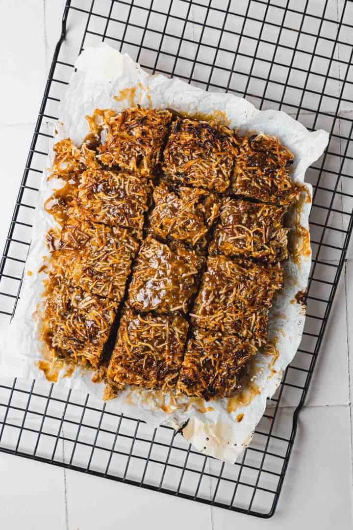 Caramel and coconut dessert bars cut into squares, cooling on a wire rack lined with parchment paper.