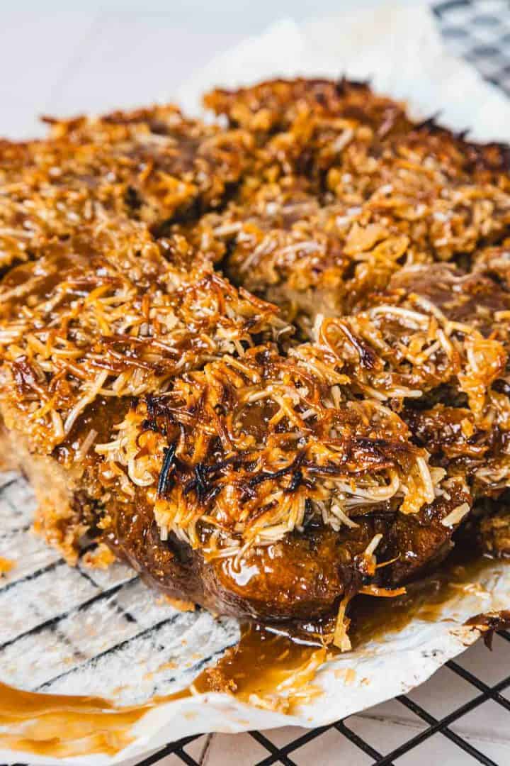Close-up of sticky, caramelized coconut dessert bars cooling on a wire rack lined with parchment paper.