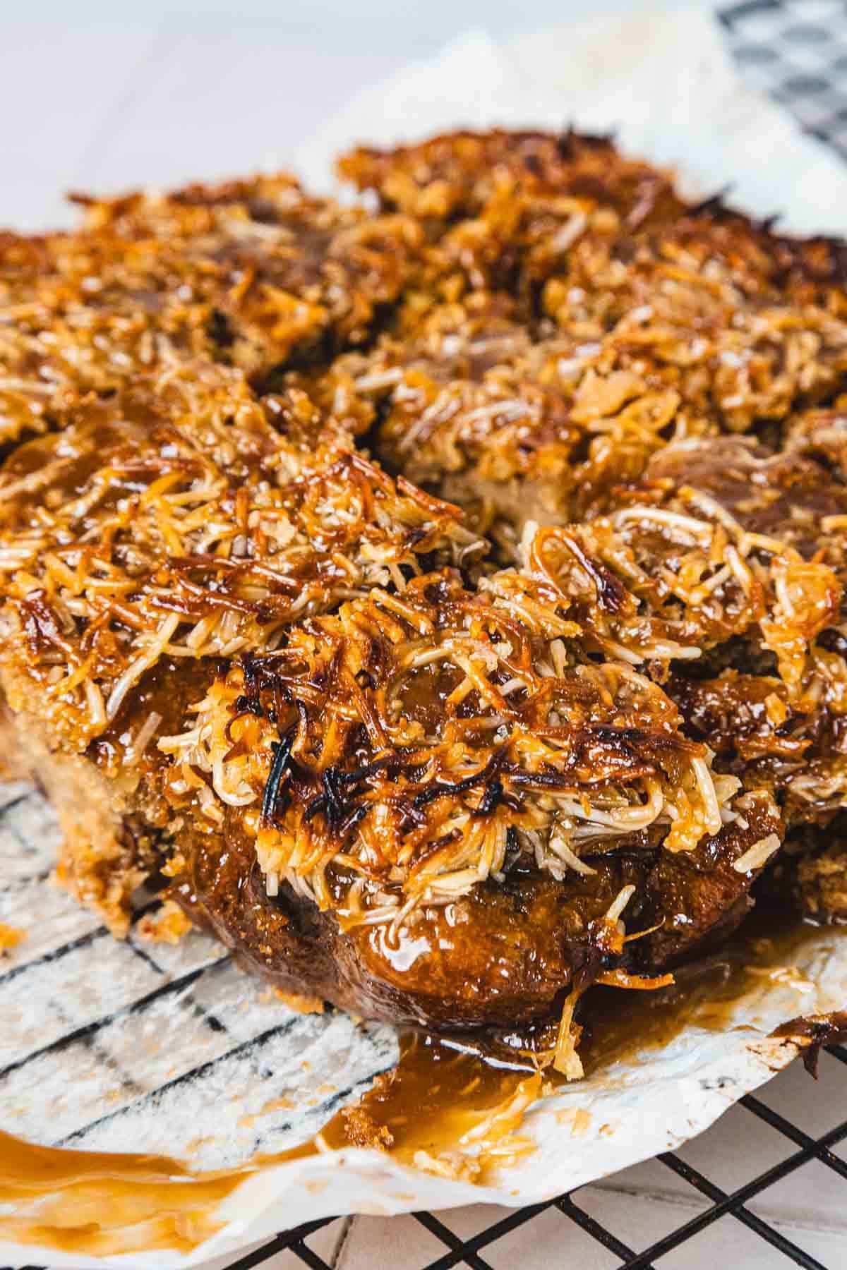 Close-up of sticky, caramelized coconut dessert bars cooling on a wire rack lined with parchment paper.