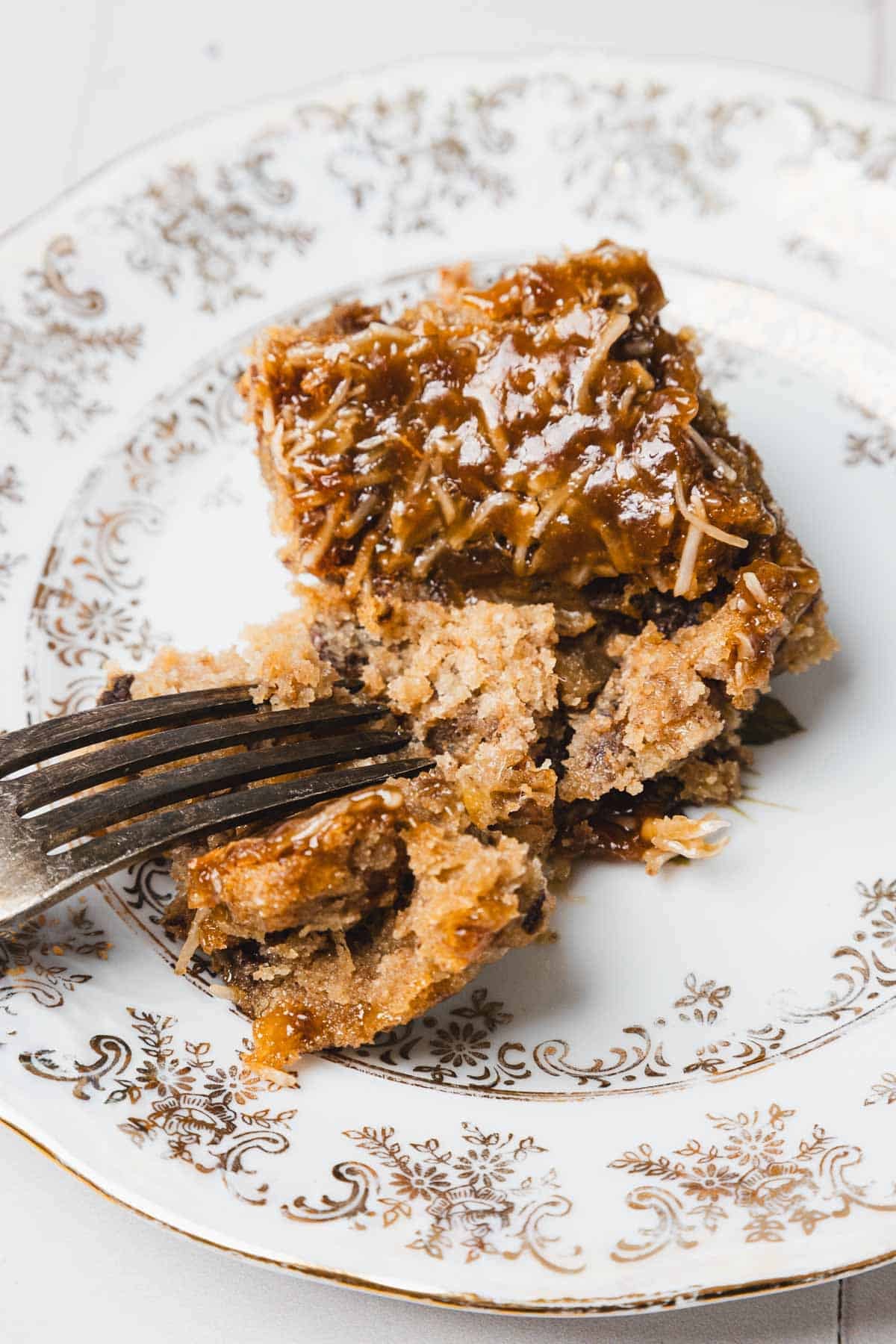 A fork cutting into a slice of moist cake with coconut and caramel topping on a decorative plate.