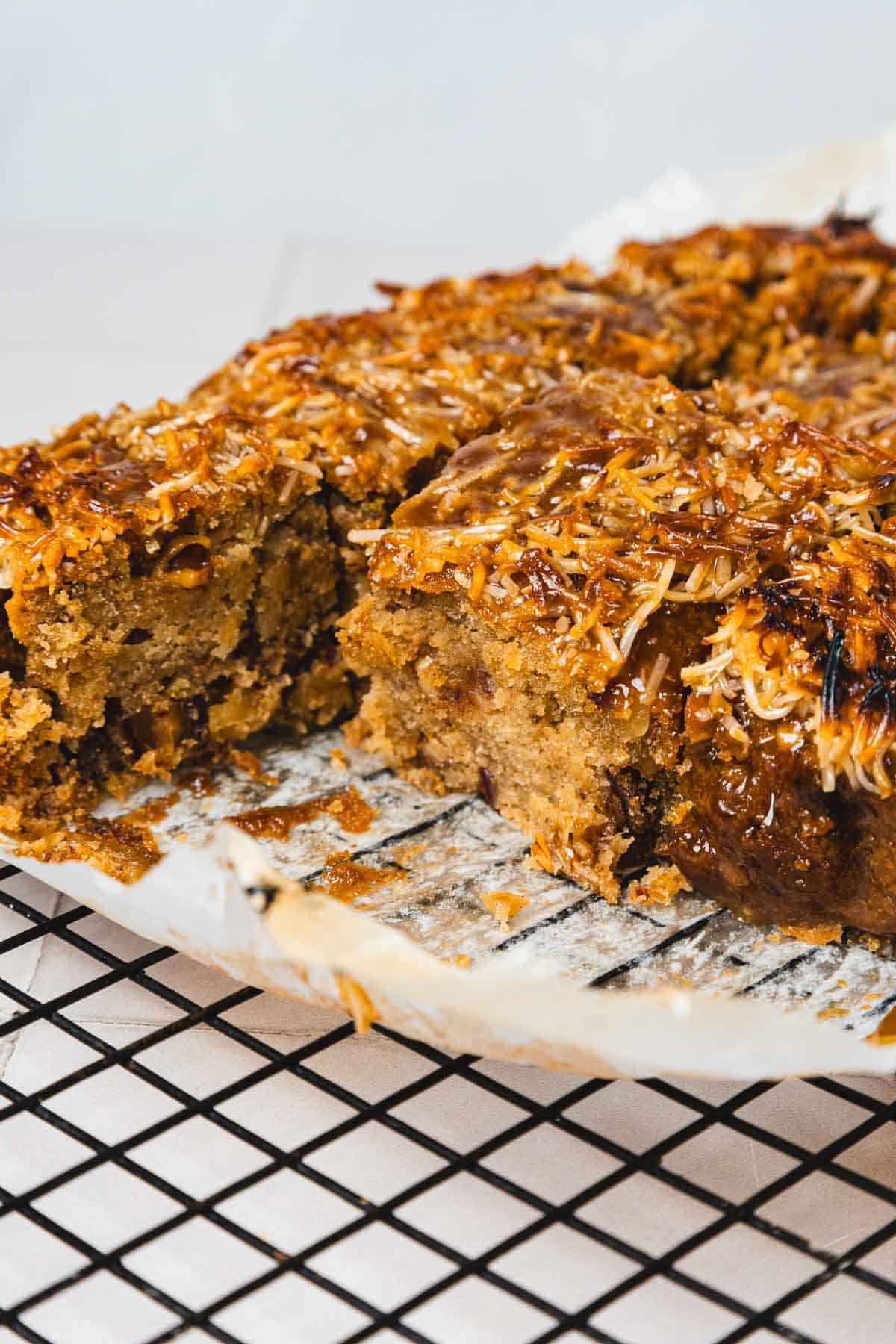 A close-up of a sliced, golden brown Queen Elizabeth Cake on parchment paper and a cooling rack.