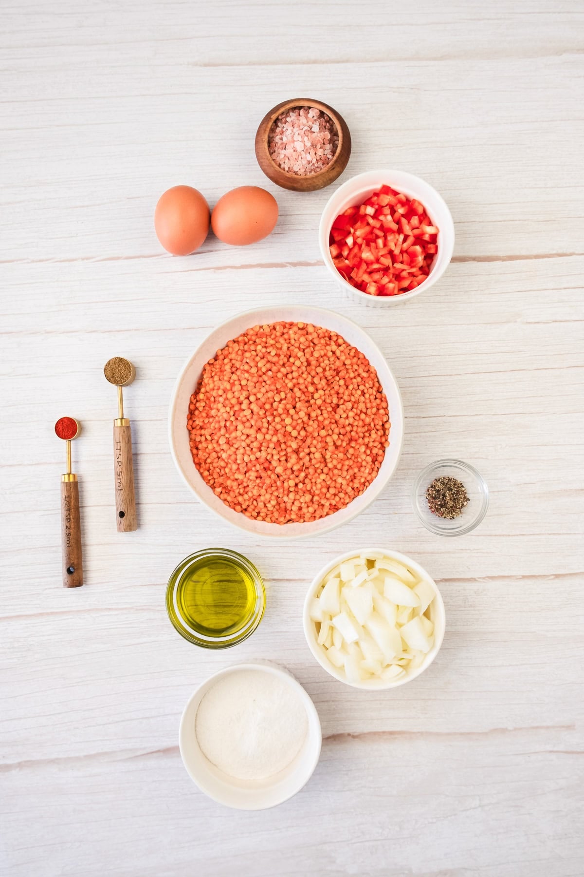 Ingredients on a table: red lentils, eggs, spices, chopped onion, diced tomato, oil, flour, and salt.