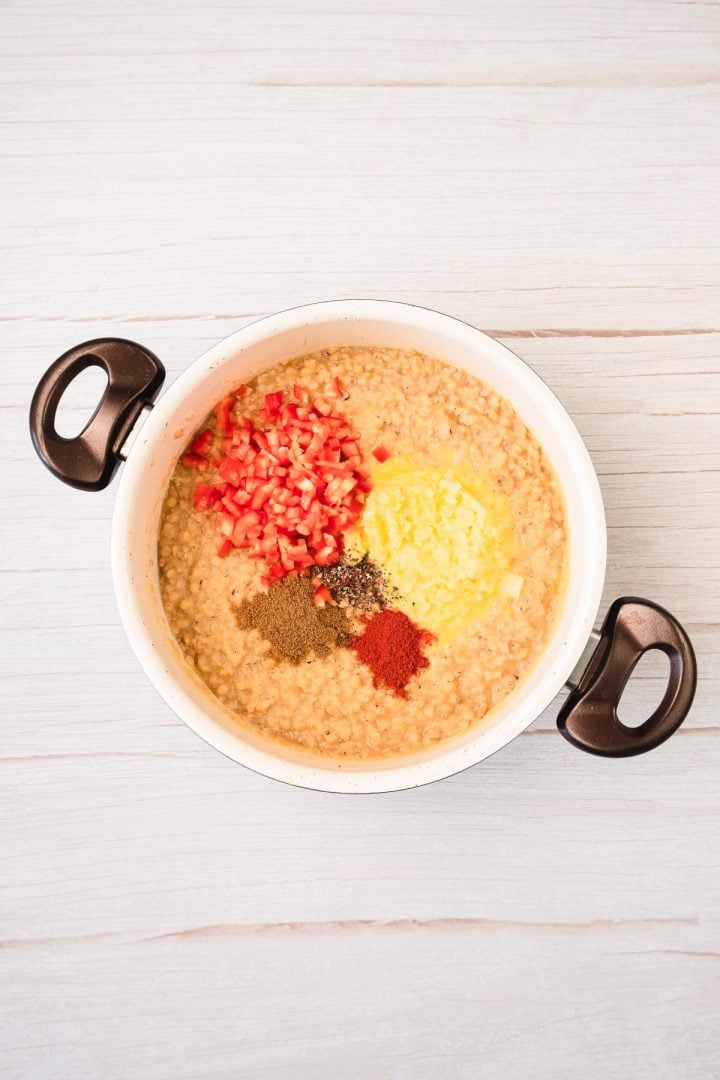 White pot with creamy mixture, chopped red peppers, yellow corn, and assorted spices on top&mdash;perfect as a filling for red lentil patties. Seen from above.