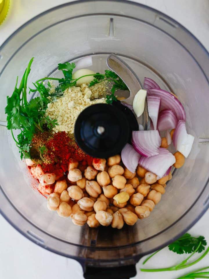 Chickpeas, red onion, garlic, spices, and herbs in a food processor ready to be blended.