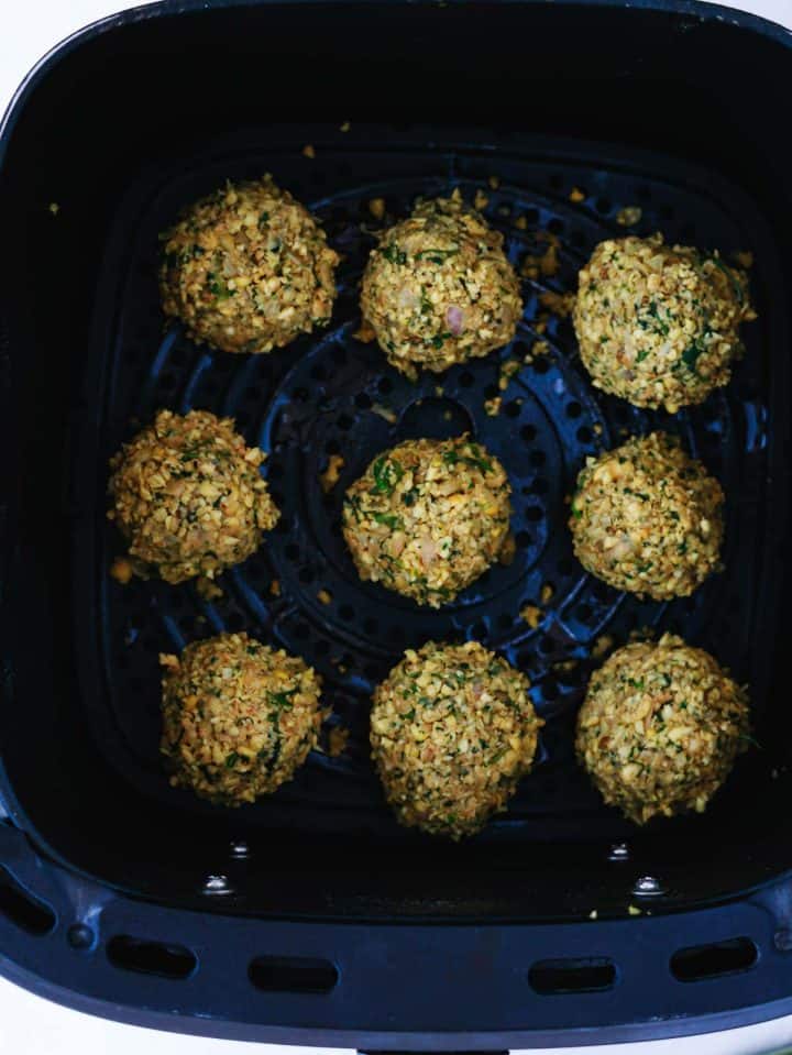 Eight uncooked falafel balls arranged in an air fryer basket, ready to be cooked.