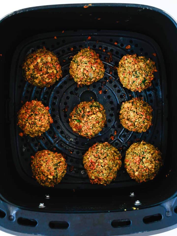 Eight baked falafel balls in an air fryer basket, arranged in a circle with one in the center.