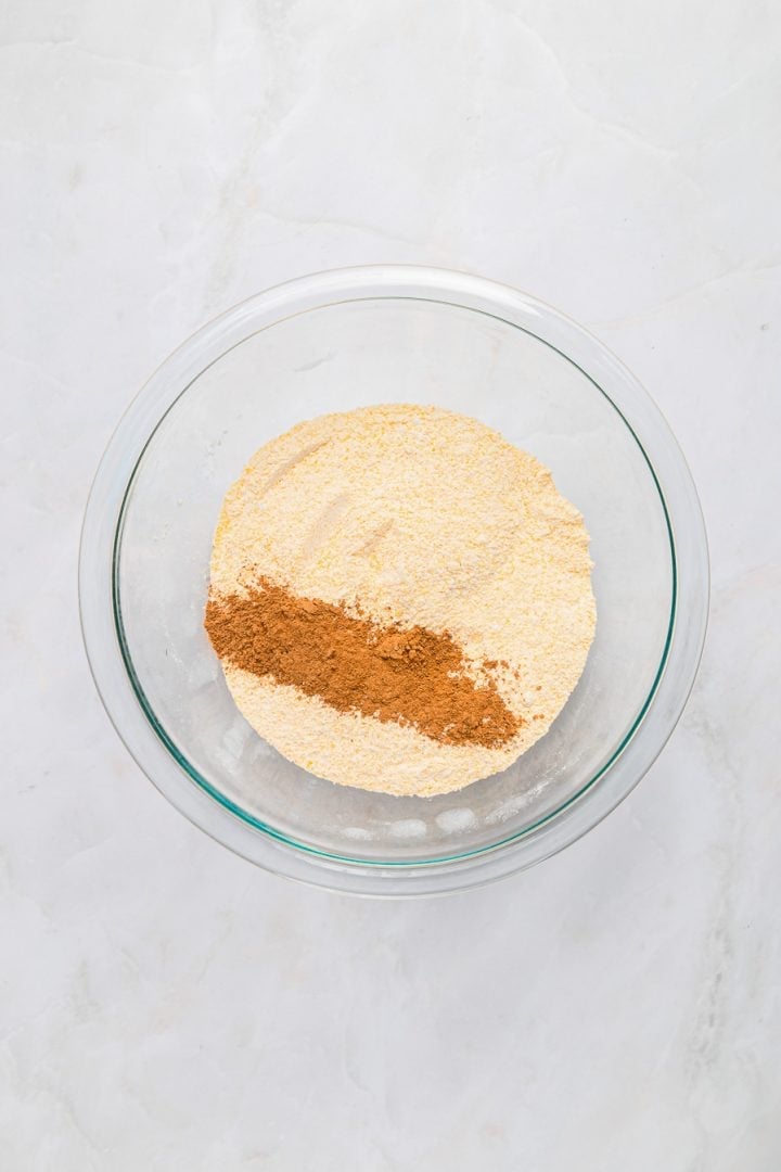 A glass bowl with cornmeal and a streak of cinnamon on a white marble surface, perfect for making Sweet Potato Cornbread.