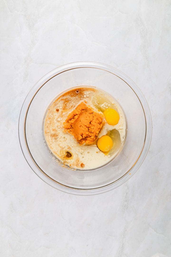 Glass bowl with eggs, pumpkin puree, and liquid ingredients on a white marble surface, ready to be mixed for Sweet Potato Cornbread.