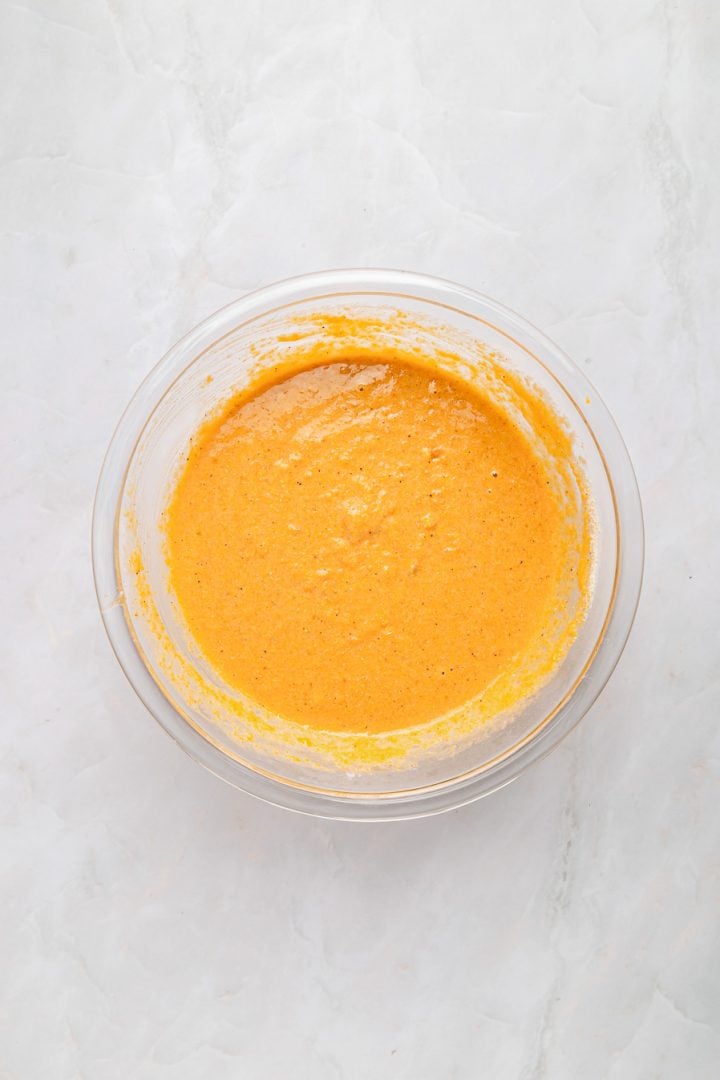 A glass bowl filled with sweet potato cornbread batter sits on a light marble surface.