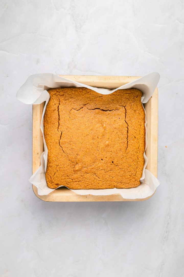 Golden brown Sweet Potato Cornbread in a parchment-lined baking pan rests on a light marble surface.