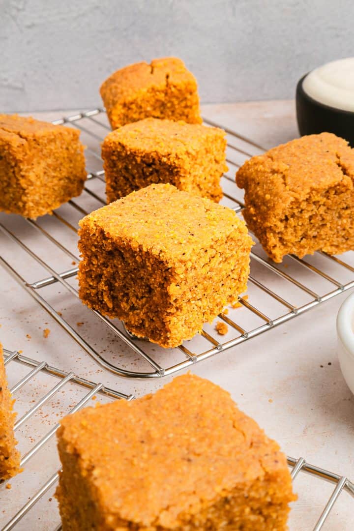 Squares of sweet potato cornbread cooling on a wire rack, with a bowl of cream in the background.