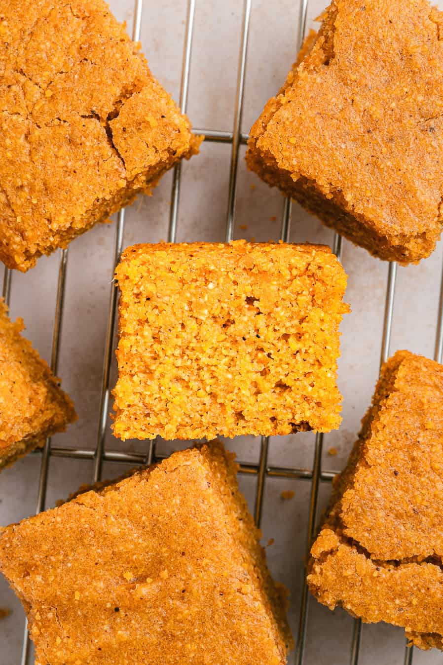 Squares of Sweet Potato Cornbread cooling on a wire rack, with one piece turned to reveal its tender crumb texture.