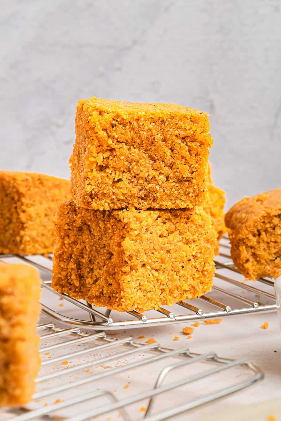 Three pieces of golden Sweet Potato Cornbread stacked on a cooling rack with a light background.