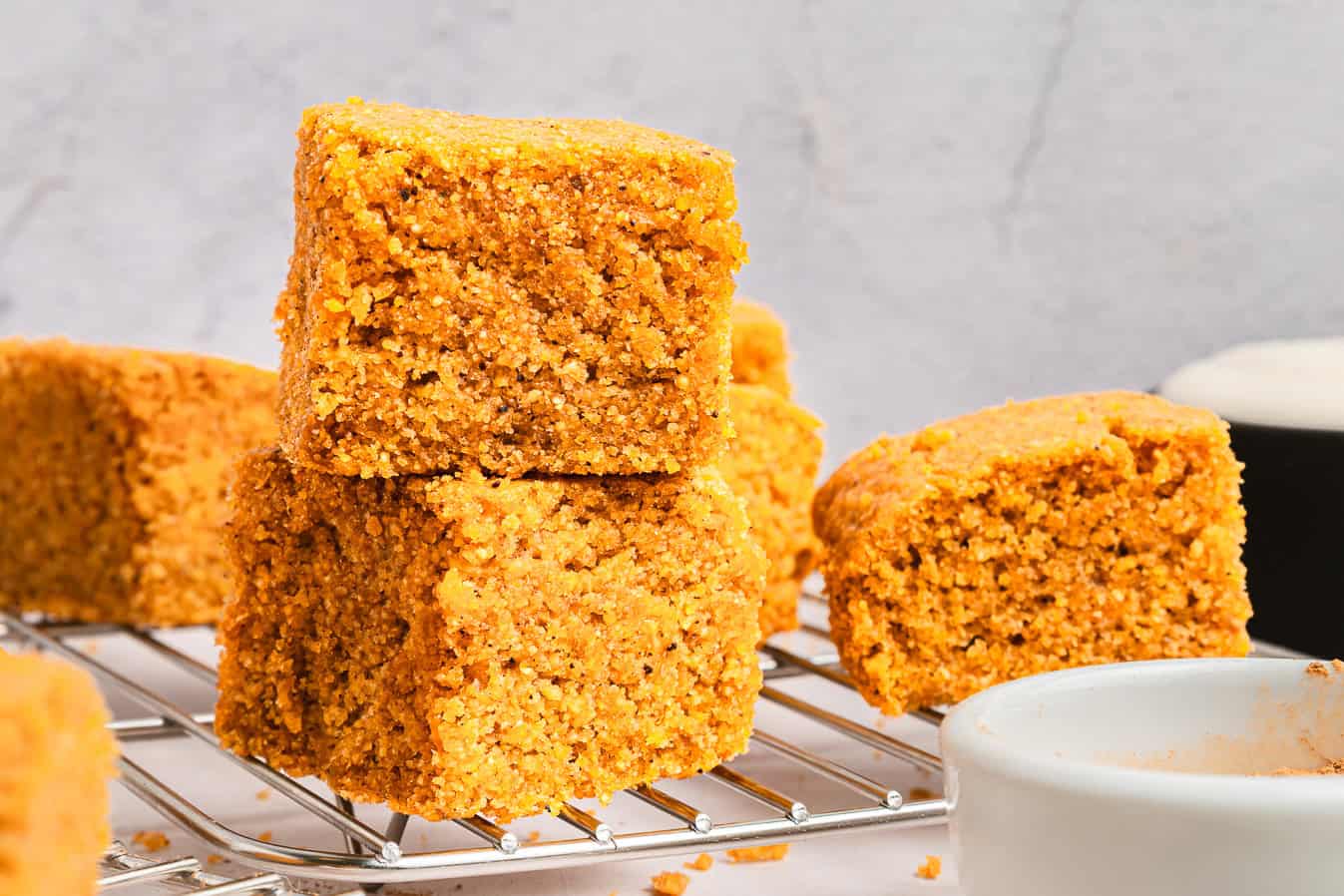 Three pieces of Sweet Potato Cornbread stacked on a cooling rack, with more delicious cornbread pieces in the background.