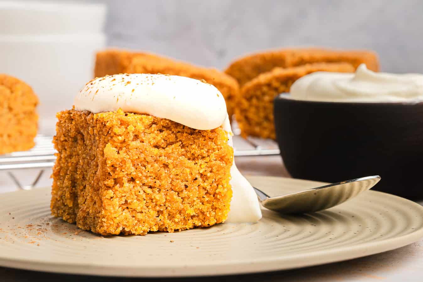 A slice of pumpkin cake topped with cream and a spoon on a plate, with more cake and Sweet Potato Cornbread in the background.