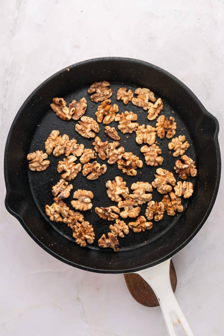 Walnut halves toasting in a black skillet on a white marble surface.