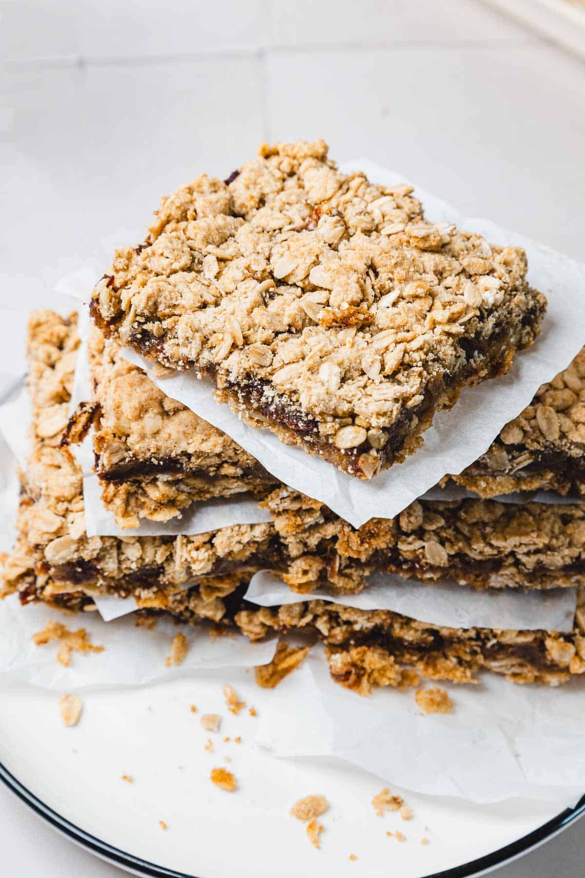 A stack of crumbly oat bars with a sweet filling, separated by parchment paper on a white plate.
