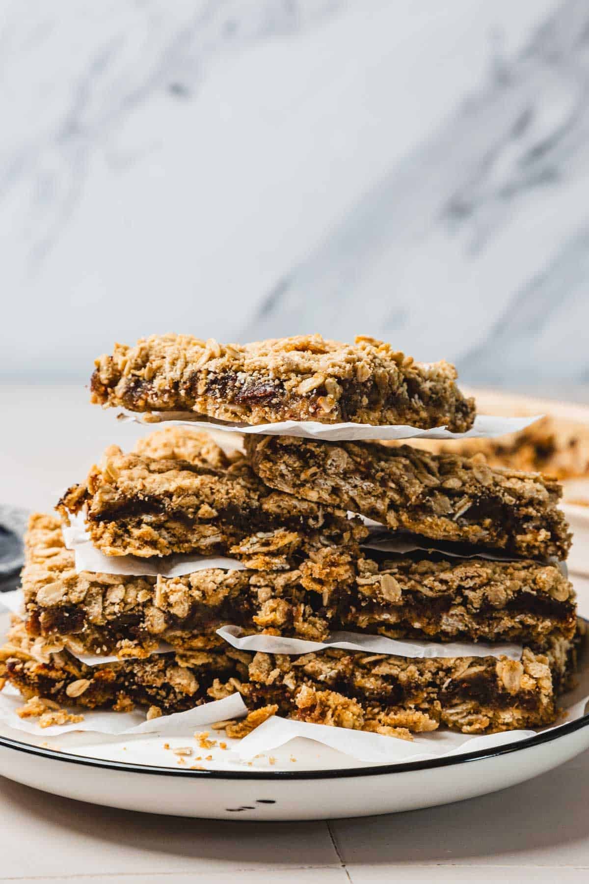 A stack of oat and date bars separated by parchment paper on a white plate.