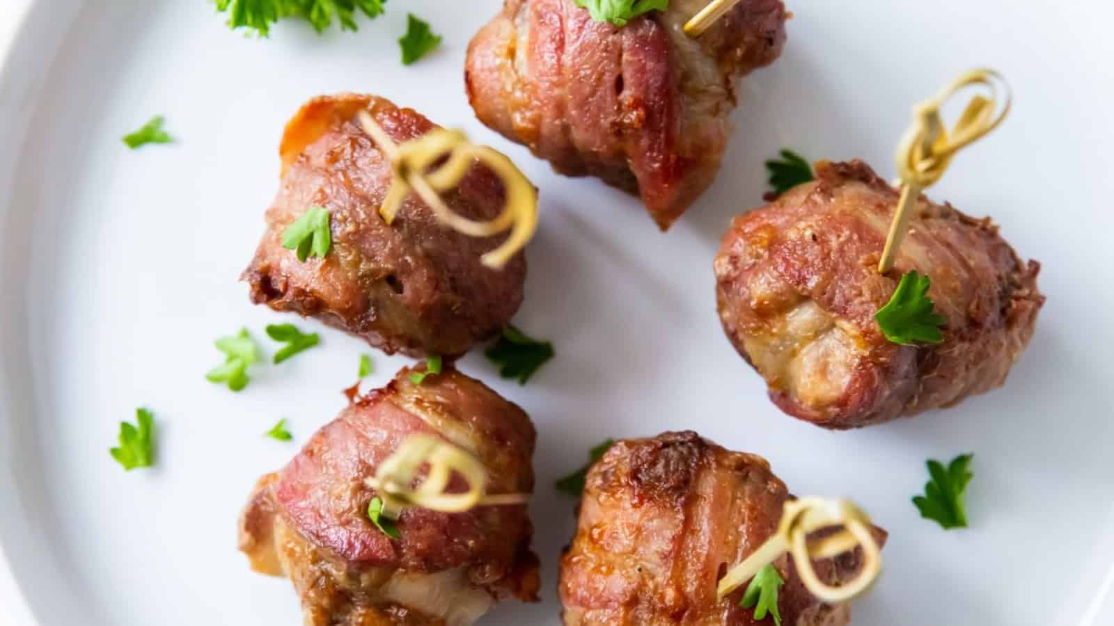 Air Fryer Bacon Wrapped Meatballs on a white plate with parsley and tooth picks.