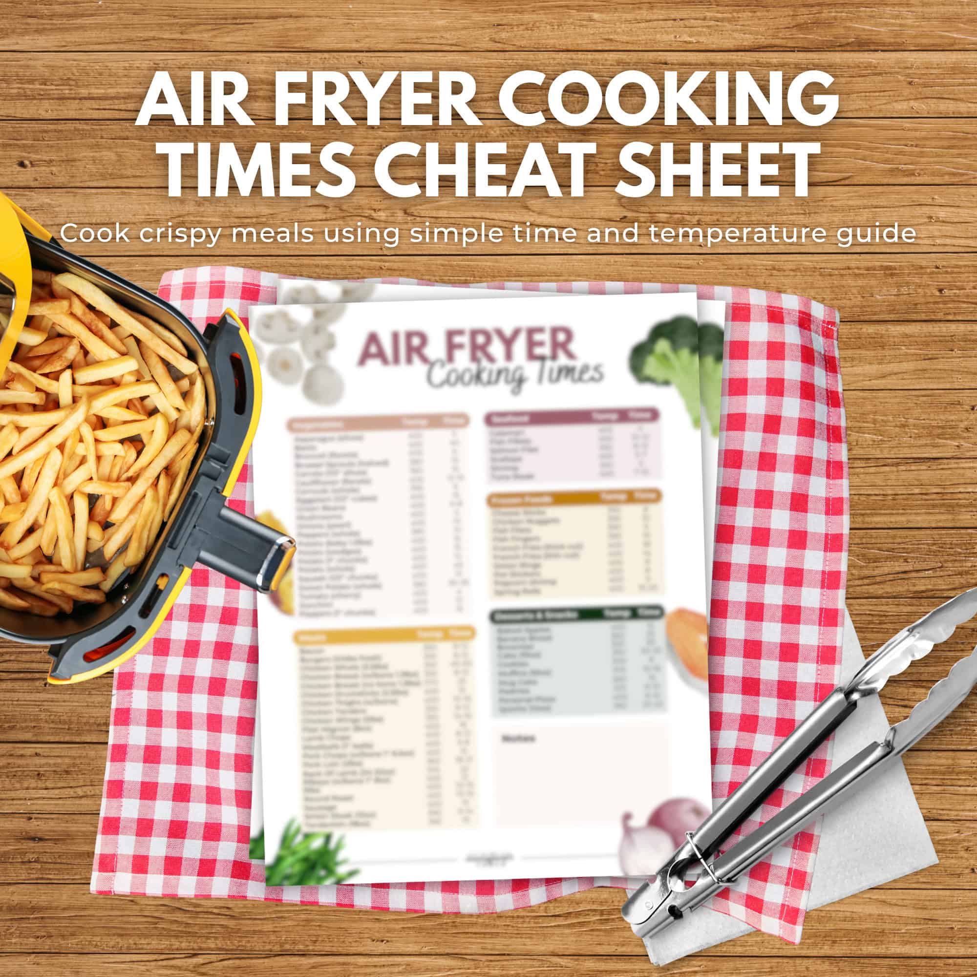 Air fryer with fries next to a printed air fryer cooking times cheat sheet from the immigrantstable shop, displayed on a red checkered cloth with tongs.