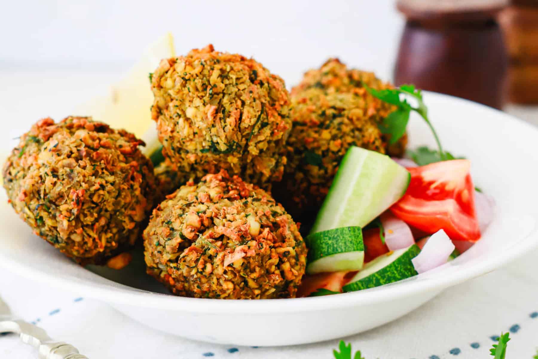 Four crispy falafel balls served with cucumber, tomato, and onion slices in a white bowl.