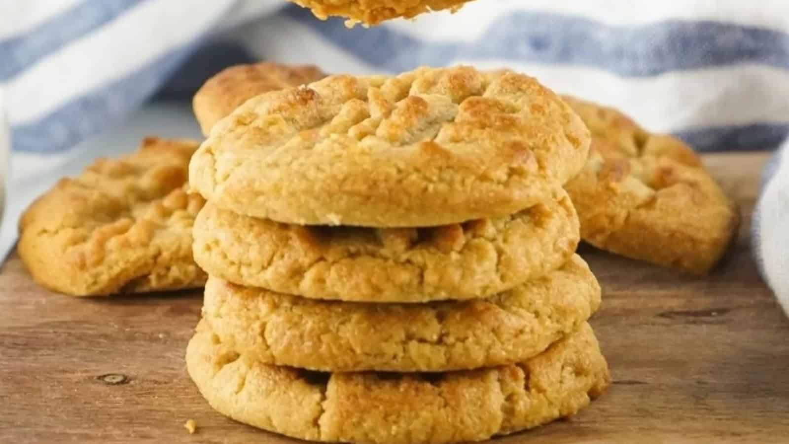 A stack of golden peanut butter cookies on a wooden surface with more cookies in the background.