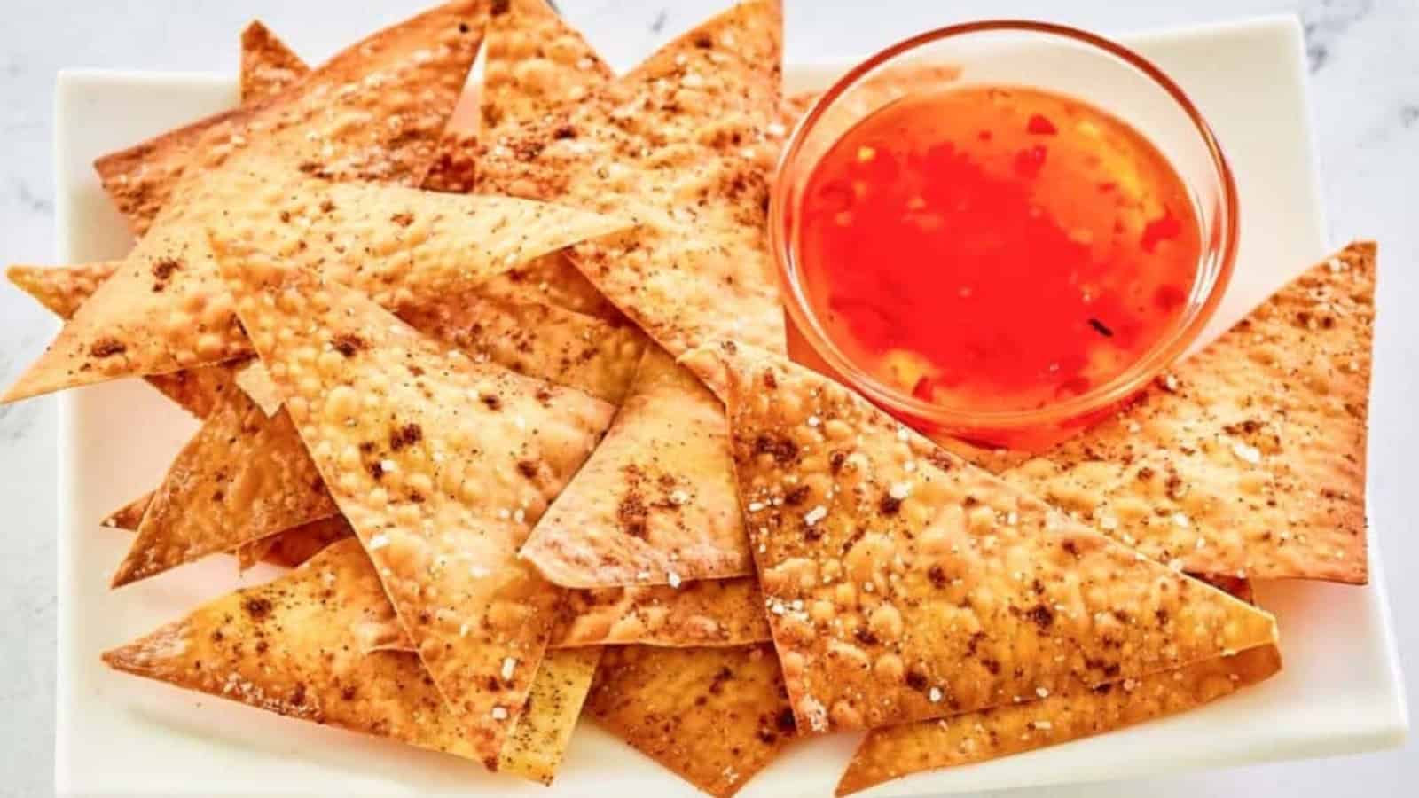 Crispy pita chips on a plate with a small bowl of bright orange dipping sauce.