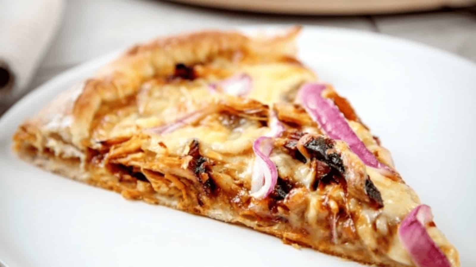 A slice of pizza topped with shredded chicken, melted cheese, and red onion on a white plate.