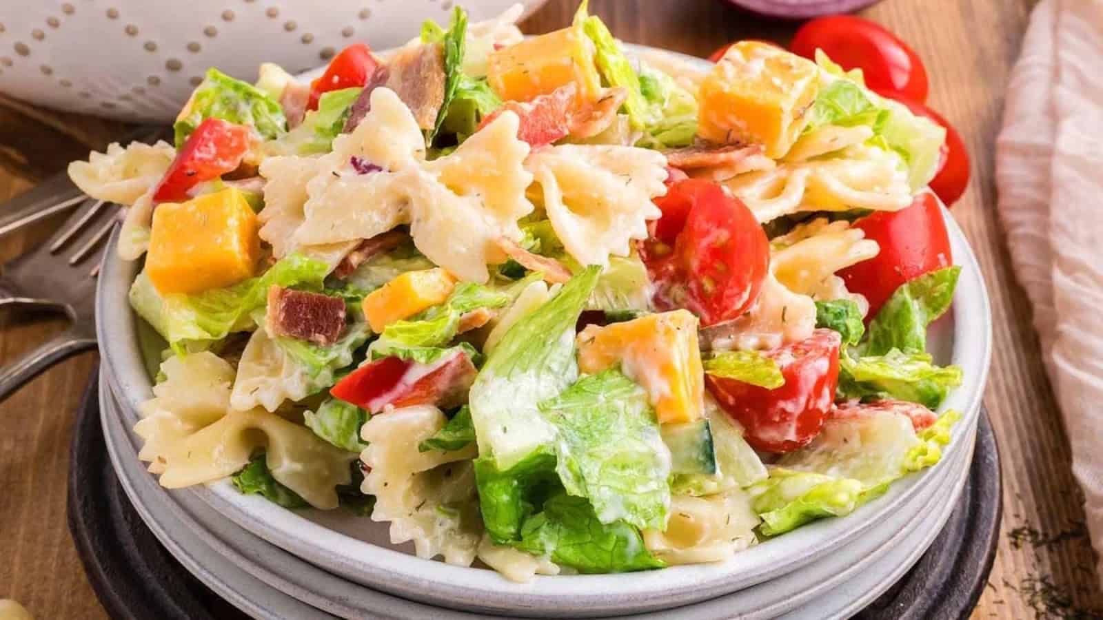 A bowl of pasta salad with bowtie pasta, lettuce, cherry tomatoes, cheese cubes, and creamy dressing.