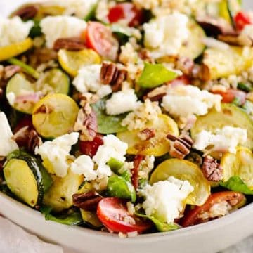 A bowl of salad with zucchini, cherry tomatoes, feta cheese, pecans, and leafy greens.