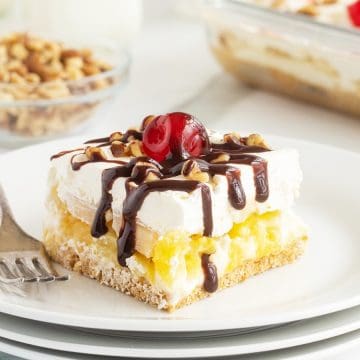 A dessert bar topped with whipped cream, chocolate drizzle, chopped nuts, and a cherry on a white plate.
