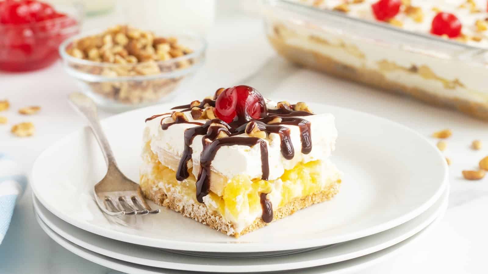 A dessert bar topped with whipped cream, chocolate drizzle, chopped nuts, and a cherry on a white plate.