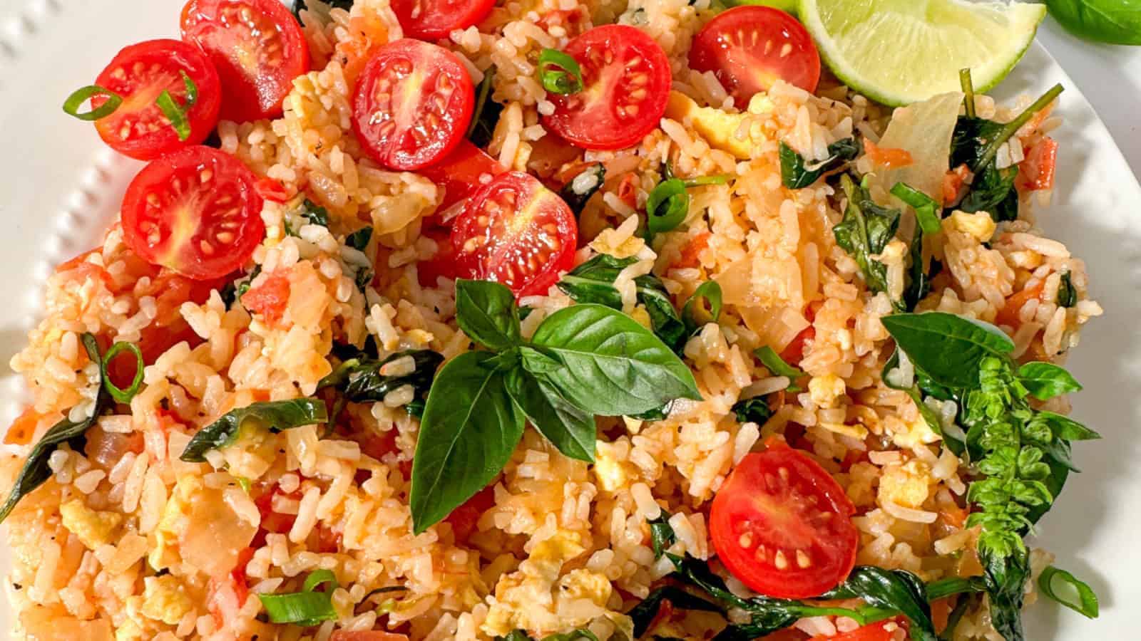 Fried rice with cherry tomatoes, leafy greens, scrambled egg, and fresh basil garnish.