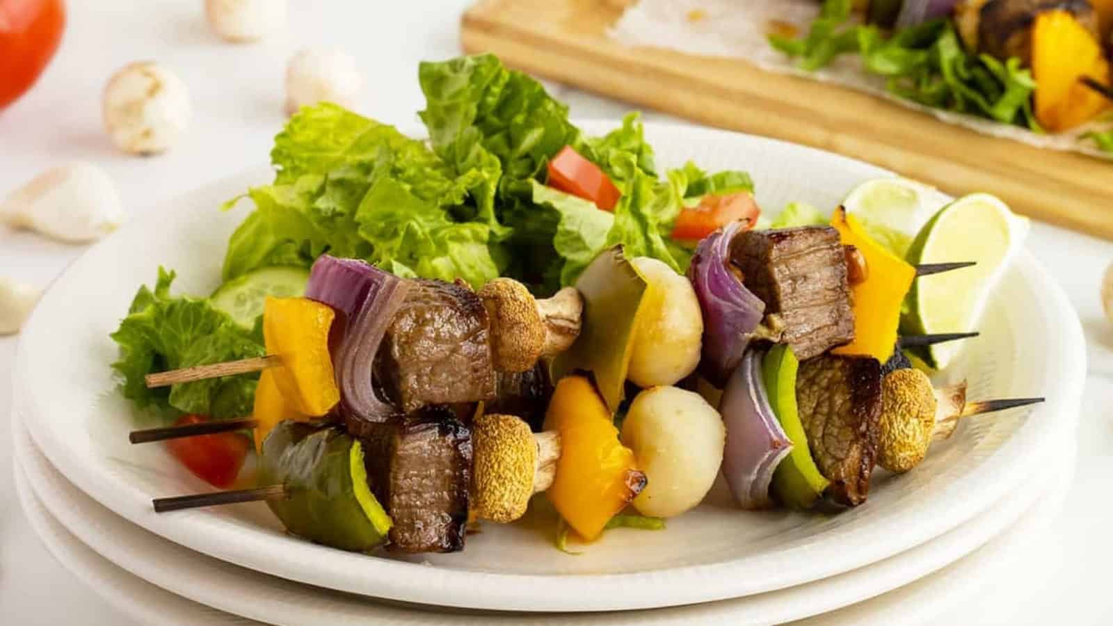 Beef and vegetable skewers served with a fresh green salad on a white plate.