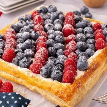 Rectangular fruit tart with blueberries and raspberries arranged in a flag pattern, dusted with powdered sugar.