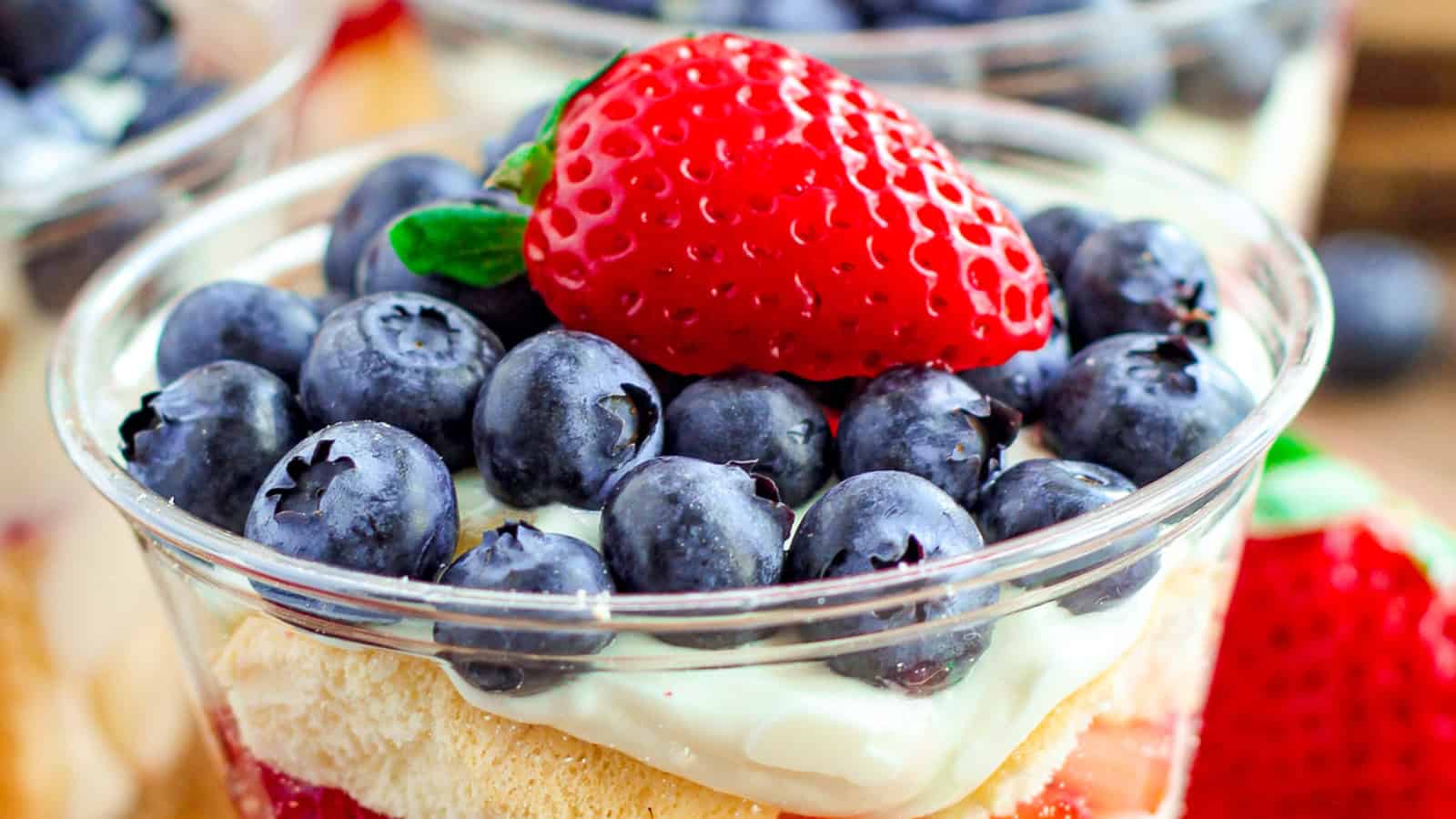 A dessert cup topped with fresh blueberries, a strawberry, whipped cream, and sponge cake layers.