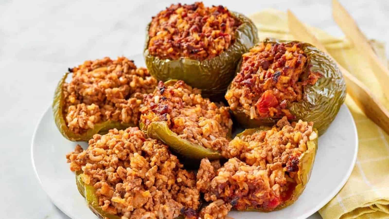 Six green bell peppers stuffed with a seasoned rice and meat mixture, served on a white plate.